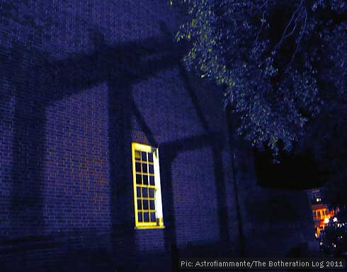 Shadow of house-like structure projected onto a brick wall with window