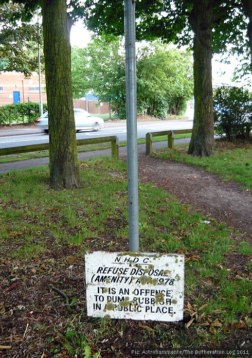 Old sign warning against dumping rubbish that has slid down its pole to ground level