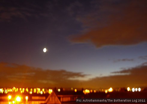 Long-exposure photograph of early evening sky, moon and clouds reflecting back streetlighting