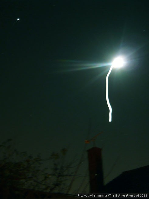 Long-exposure image of the moon with light leakage causing a long vertical trail away from the main light source