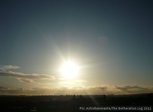 Blue sky with clouds on horizon and bright sun in the centre of the image