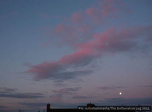 The moon heading down to the horizon below pink and blue clouds