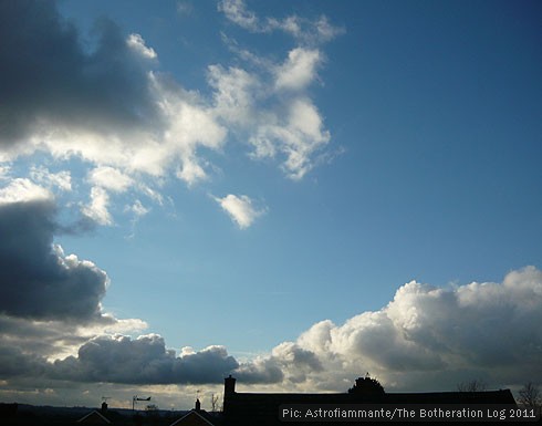 Rolling cumulus clouds against a blue sky, over rooftops