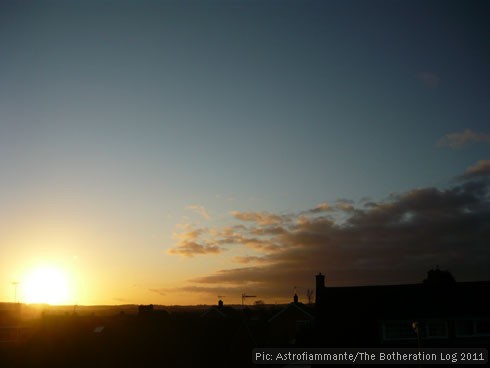 Sun about to set below horizon, against dark-blue sky and grey cloud