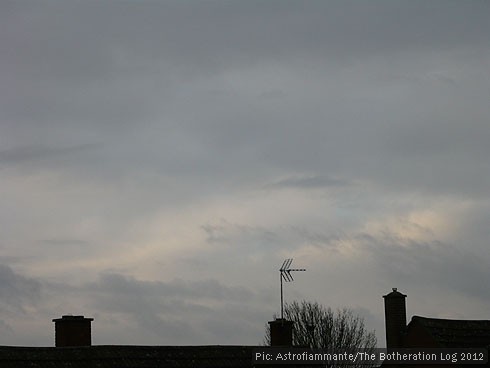 Sillhouetted trees and chimneys against a dark, cloudy sky