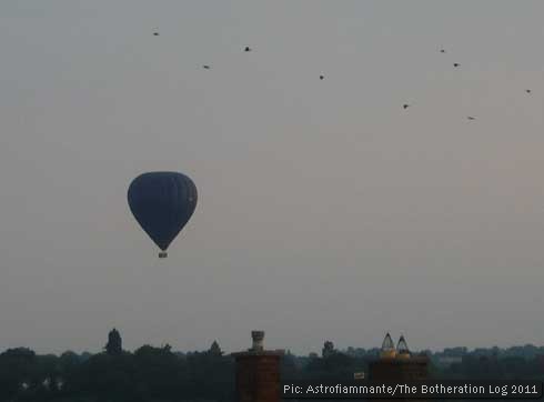 Hot air balloon floating over hills and rooftops with a flock of birds